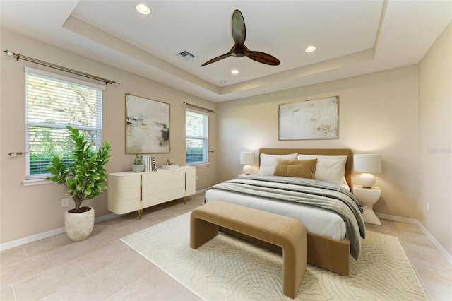 tiled bedroom with multiple windows, a tray ceiling, and ceiling fan