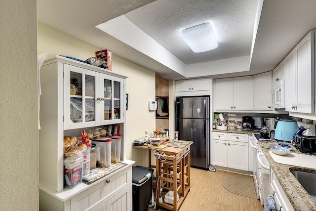 kitchen with light stone counters, black fridge, white cabinetry, light hardwood / wood-style flooring, and a raised ceiling