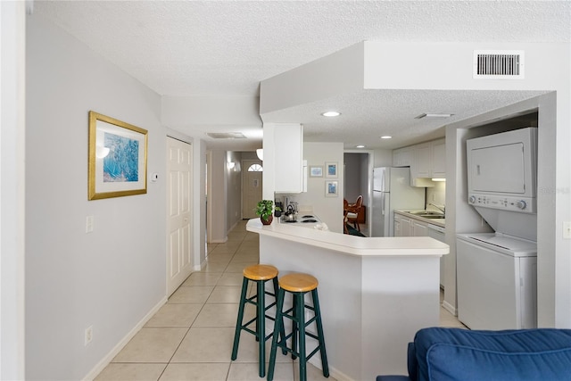 kitchen featuring kitchen peninsula, stacked washer and clothes dryer, a textured ceiling, white cabinetry, and a kitchen breakfast bar