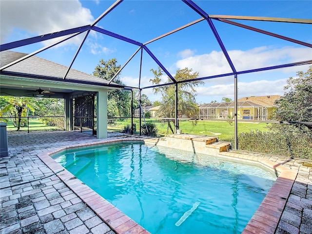 view of swimming pool with glass enclosure, a yard, ceiling fan, and a patio area