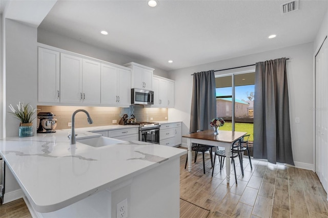 kitchen featuring sink, stainless steel appliances, light hardwood / wood-style flooring, kitchen peninsula, and white cabinets