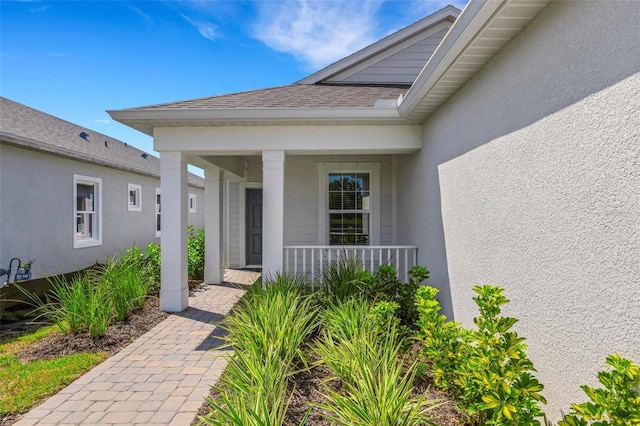 property entrance with stucco siding, a porch, and roof with shingles