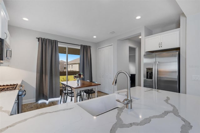 kitchen featuring white cabinets, stainless steel appliances, light stone counters, and sink