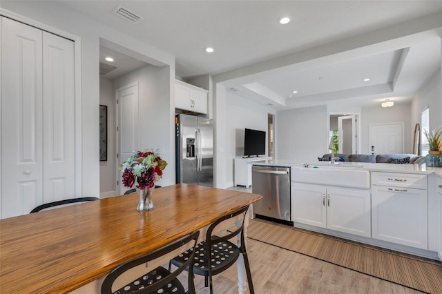 kitchen featuring a tray ceiling, white cabinets, light hardwood / wood-style floors, and appliances with stainless steel finishes