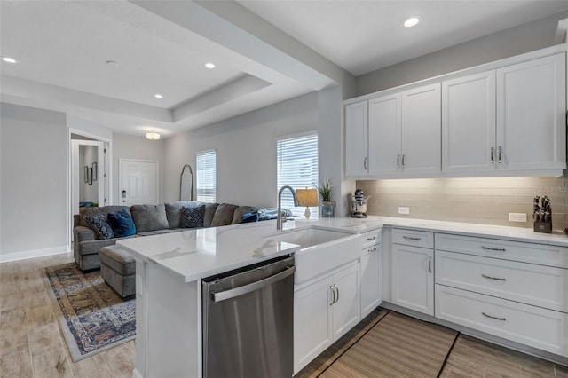 kitchen featuring a raised ceiling, stainless steel dishwasher, open floor plan, a sink, and a peninsula