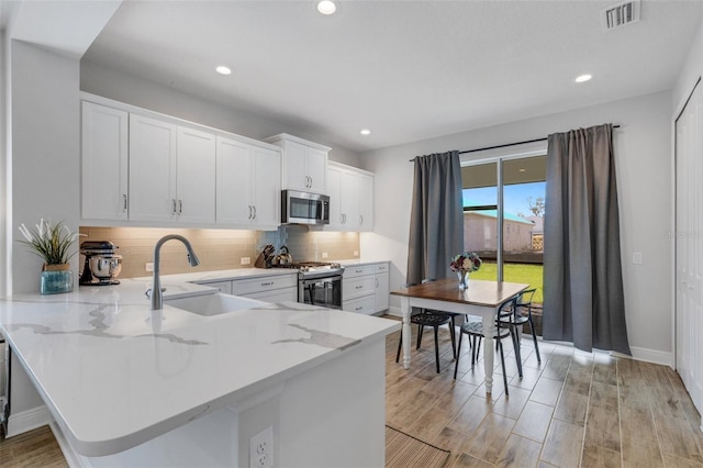 kitchen with stainless steel appliances, tasteful backsplash, visible vents, white cabinets, and a sink