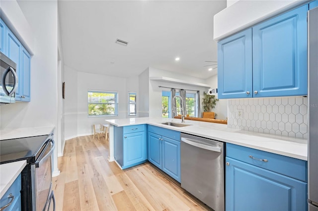 kitchen featuring blue cabinets, light hardwood / wood-style floors, stainless steel appliances, and kitchen peninsula