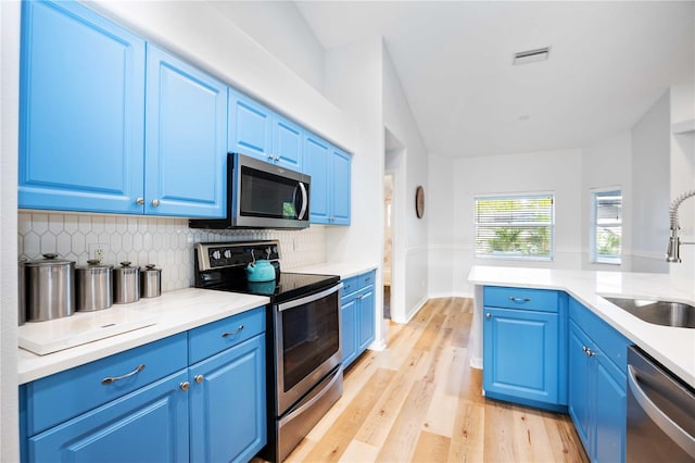 kitchen with sink, tasteful backsplash, blue cabinetry, appliances with stainless steel finishes, and light wood-type flooring