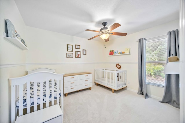 carpeted bedroom with ceiling fan and a nursery area