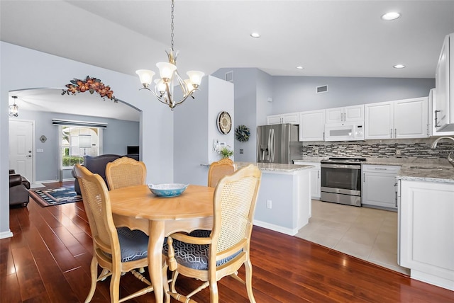 dining space with a notable chandelier, light hardwood / wood-style flooring, sink, and vaulted ceiling