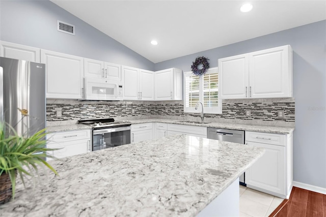 kitchen with white cabinets, lofted ceiling, sink, stainless steel appliances, and decorative backsplash