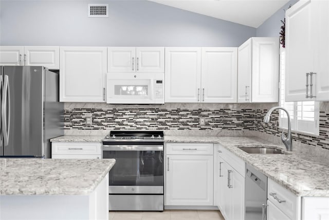 kitchen with white cabinets, sink, stainless steel appliances, light stone countertops, and vaulted ceiling