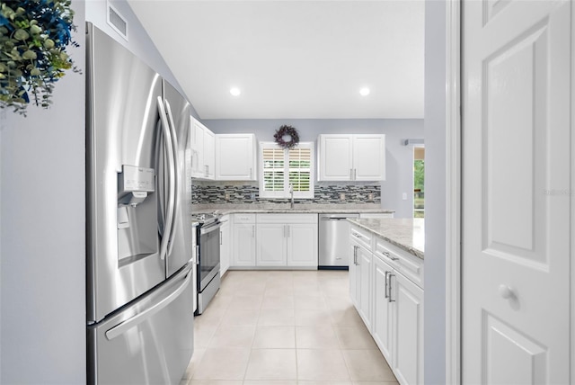 kitchen featuring white cabinets, light tile patterned flooring, appliances with stainless steel finishes, light stone countertops, and decorative backsplash