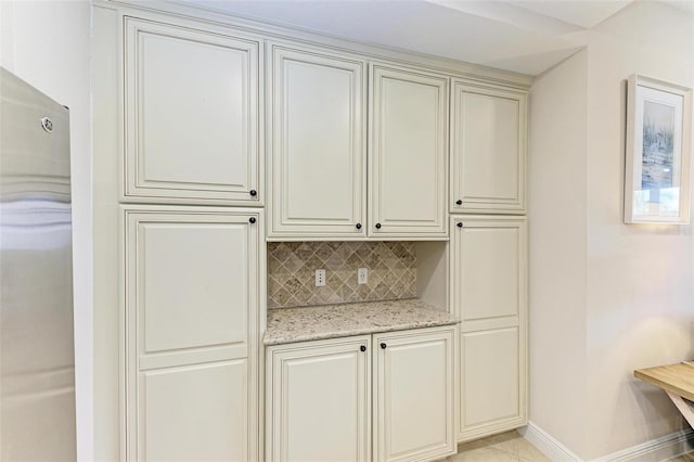 interior space with backsplash, light stone counters, light tile patterned floors, and cream cabinetry