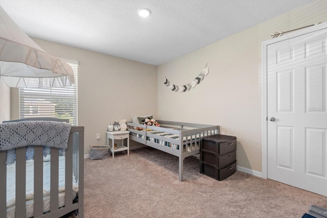 carpeted bedroom featuring a textured ceiling and a nursery area