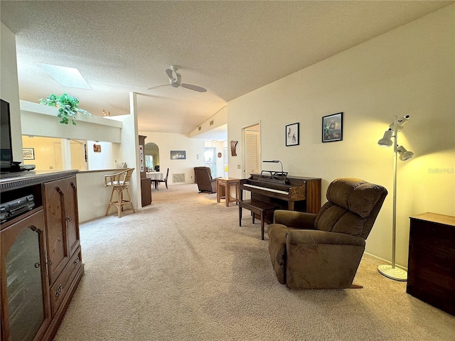 living room featuring vaulted ceiling with skylight, ceiling fan, light colored carpet, and a textured ceiling