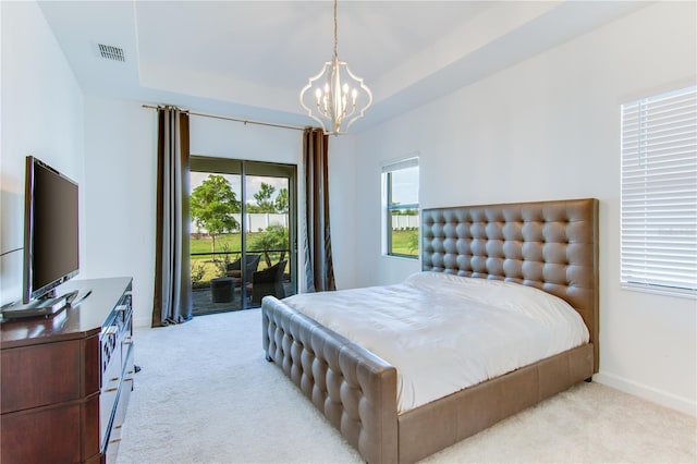 carpeted bedroom featuring a tray ceiling, access to exterior, and a chandelier