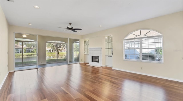 unfurnished living room featuring a tile fireplace, ceiling fan, and hardwood / wood-style floors