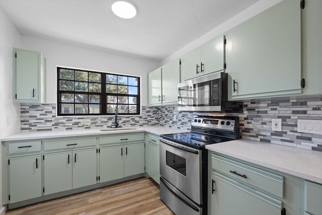 kitchen with appliances with stainless steel finishes, backsplash, sink, and light hardwood / wood-style flooring