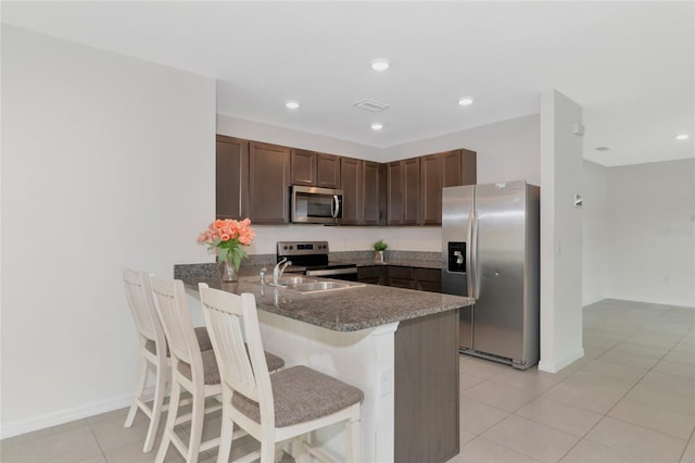 kitchen with light tile patterned floors, kitchen peninsula, dark brown cabinets, stainless steel appliances, and a kitchen bar