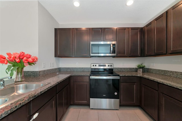 kitchen featuring dark brown cabinetry, light tile patterned floors, sink, stainless steel appliances, and dark stone counters