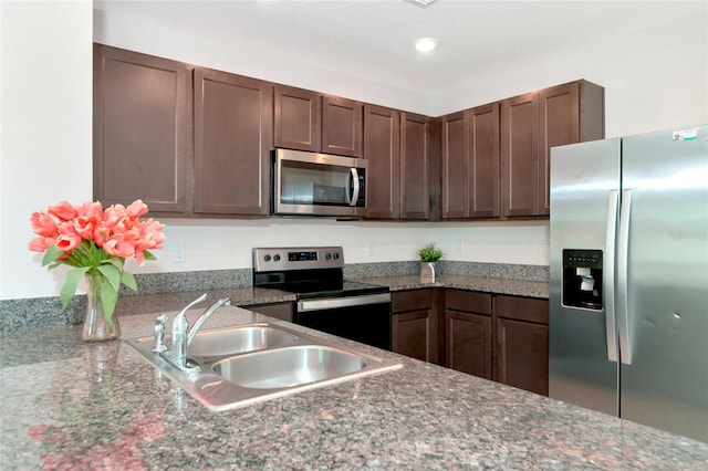 kitchen featuring dark brown cabinetry, stainless steel appliances, sink, and dark stone counters