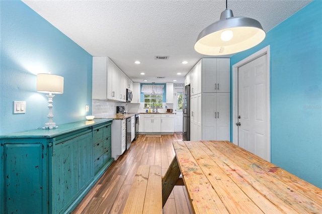 kitchen featuring pendant lighting, tasteful backsplash, a textured ceiling, white cabinetry, and dark hardwood / wood-style floors