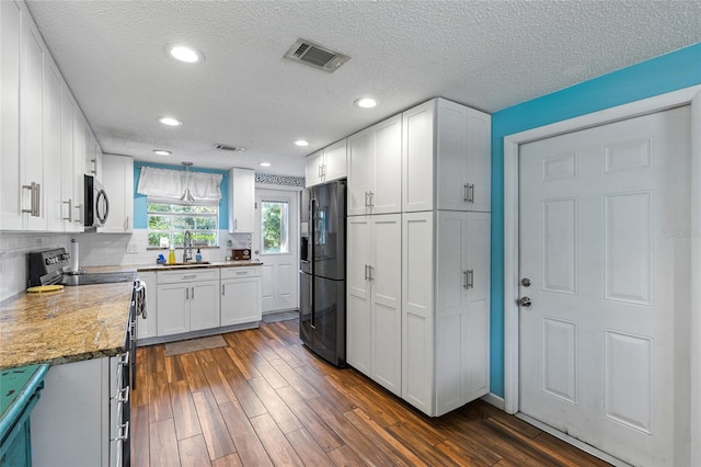 kitchen featuring a textured ceiling, appliances with stainless steel finishes, dark wood-type flooring, and white cabinetry