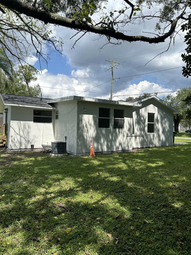 back of property with central AC unit and a yard