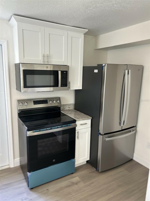 kitchen featuring white cabinets, a textured ceiling, stainless steel appliances, and light wood-type flooring