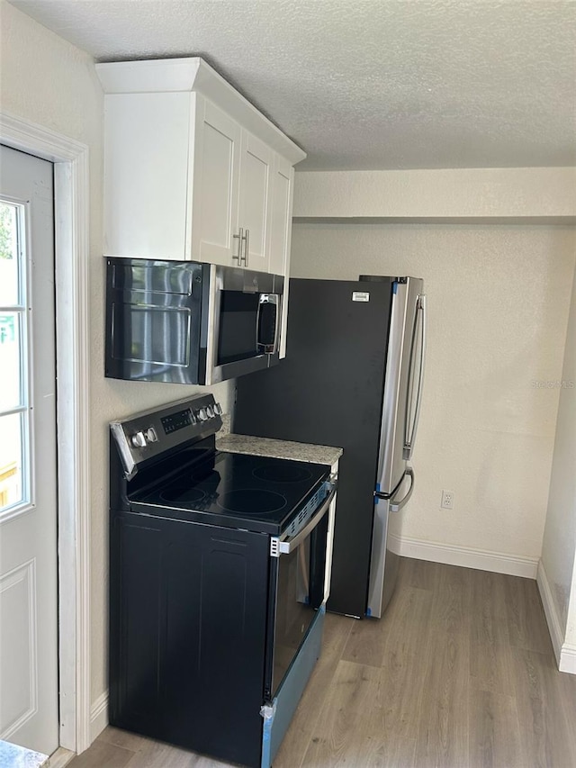 kitchen with light hardwood / wood-style flooring, white cabinets, a textured ceiling, and appliances with stainless steel finishes