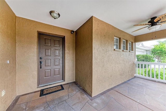 view of exterior entry with ceiling fan and a porch