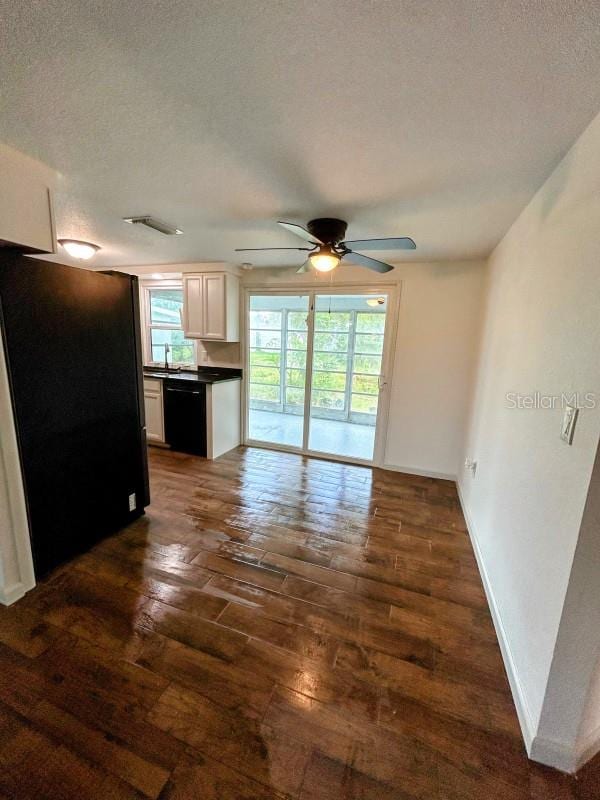 unfurnished living room with a textured ceiling, a healthy amount of sunlight, dark hardwood / wood-style flooring, and ceiling fan