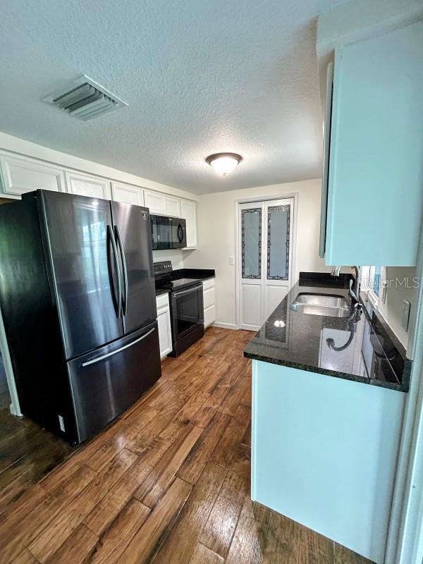 kitchen featuring a textured ceiling, sink, white cabinets, black appliances, and dark hardwood / wood-style flooring