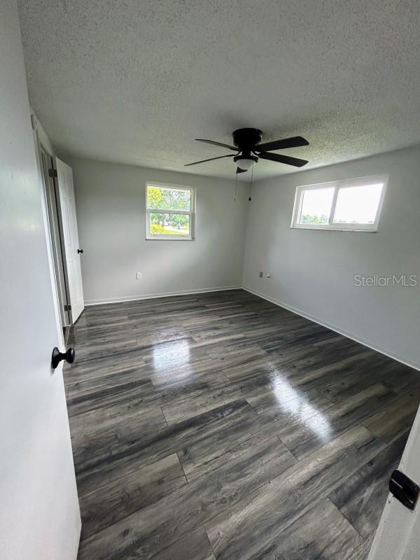 empty room with ceiling fan, a textured ceiling, and dark wood-type flooring