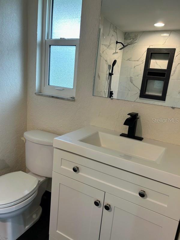 bathroom featuring a tile shower, vanity, and toilet