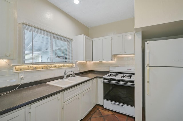 kitchen with tasteful backsplash, white cabinets, white appliances, dark tile patterned floors, and sink