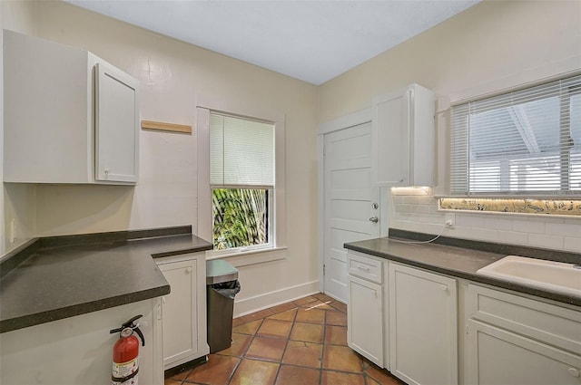 kitchen featuring backsplash, sink, dark tile patterned floors, and white cabinets