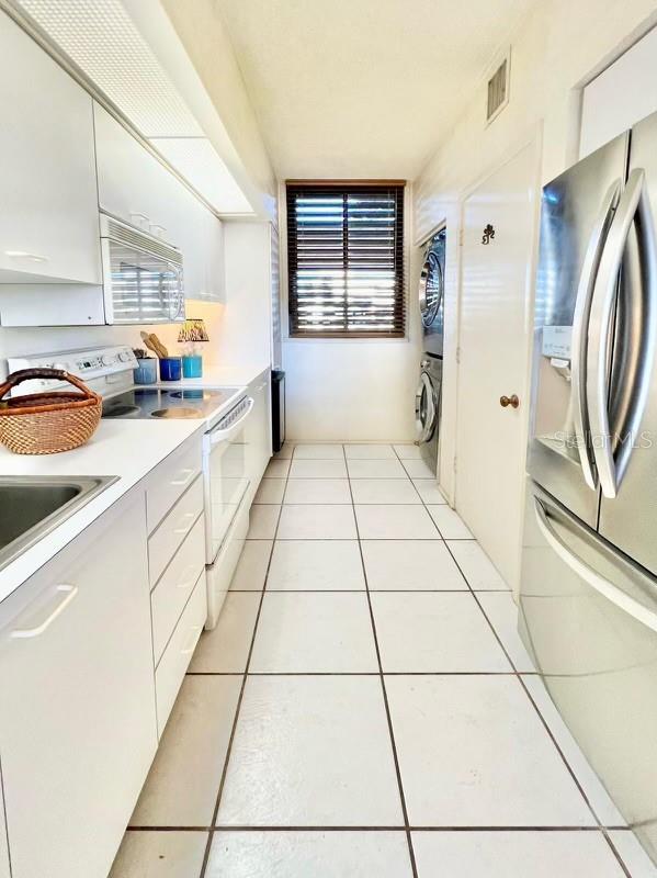 kitchen with white cabinets, light tile patterned floors, white appliances, stacked washer and clothes dryer, and plenty of natural light