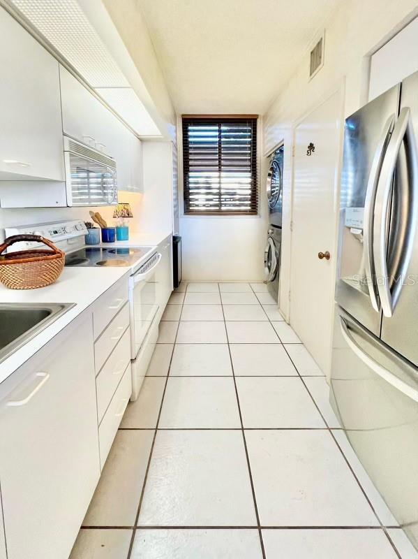 kitchen featuring stacked washer and clothes dryer, white appliances, light tile patterned floors, white cabinetry, and visible vents