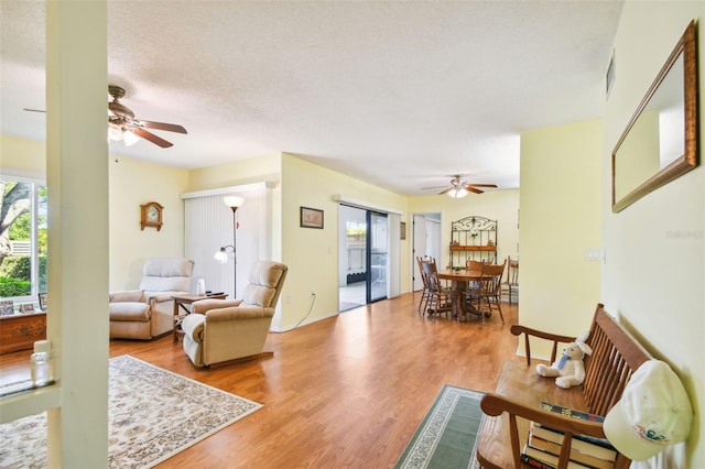 living room featuring light hardwood / wood-style floors, ceiling fan, and a textured ceiling