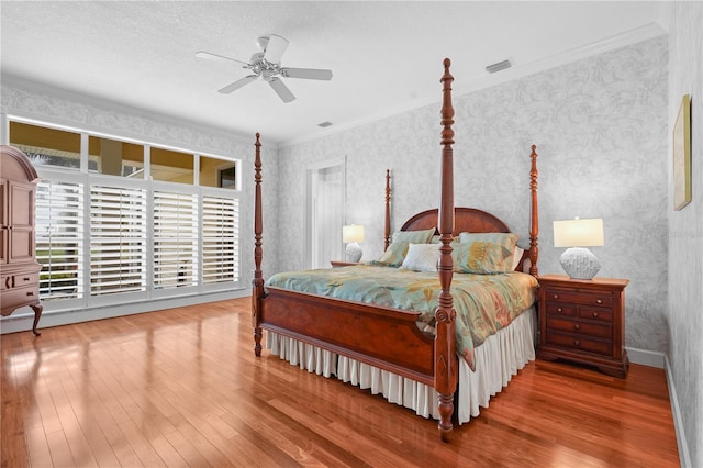 bedroom featuring baseboards, crown molding, hardwood / wood-style floors, and wallpapered walls