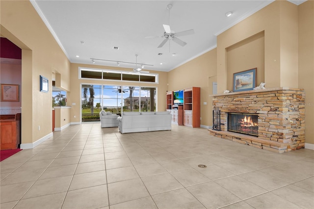 living room featuring light tile patterned floors, baseboards, ornamental molding, and a stone fireplace