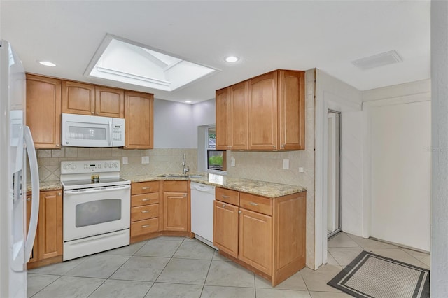 kitchen featuring light stone counters, light tile patterned flooring, sink, white appliances, and a skylight