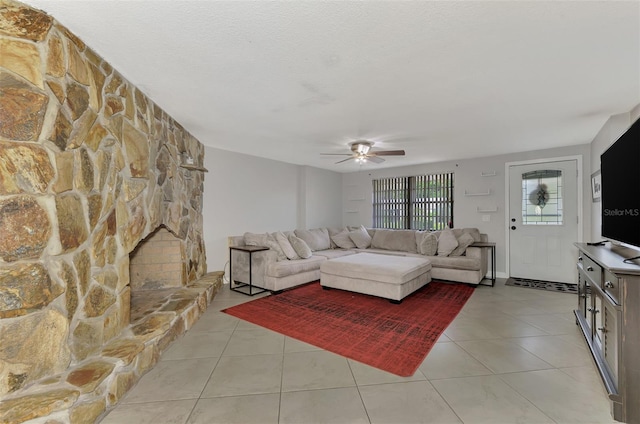 living room featuring a textured ceiling, light tile patterned floors, a stone fireplace, and ceiling fan