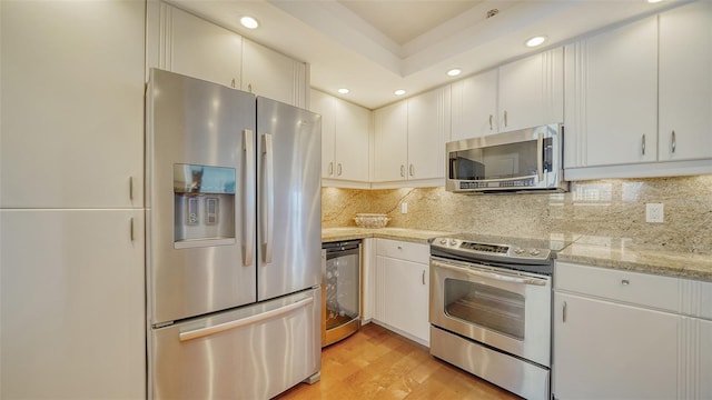 kitchen with light hardwood / wood-style flooring, white cabinetry, appliances with stainless steel finishes, and backsplash