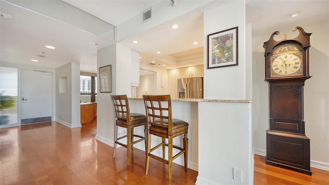 kitchen featuring a kitchen breakfast bar, light wood-type flooring, kitchen peninsula, and stainless steel fridge