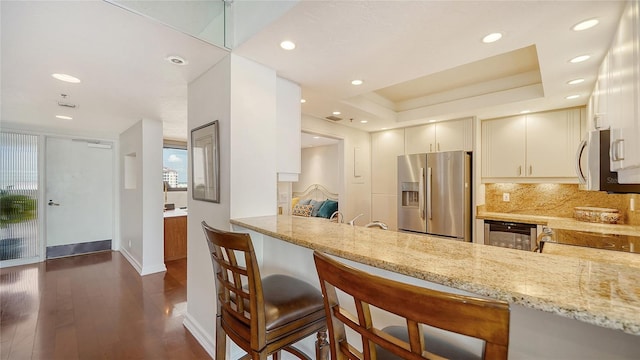 kitchen featuring appliances with stainless steel finishes, a kitchen bar, light stone countertops, and kitchen peninsula