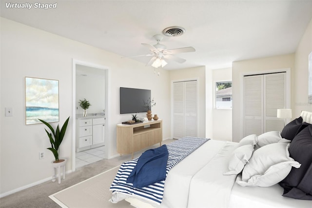 carpeted bedroom with connected bathroom, multiple closets, and ceiling fan