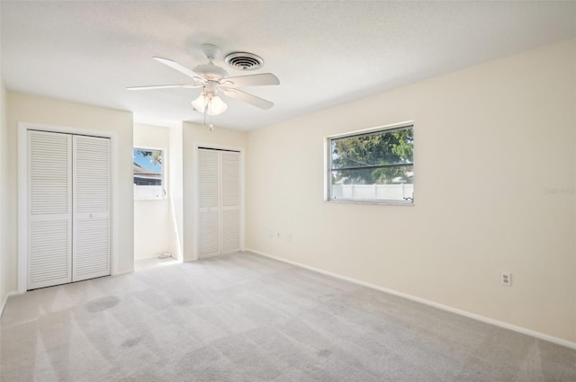 unfurnished bedroom with light carpet, two closets, and ceiling fan